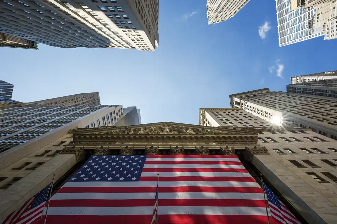 Fachada da Bolsa de Valores de Nova York coberta pela bandeira dos Estados Unidos.